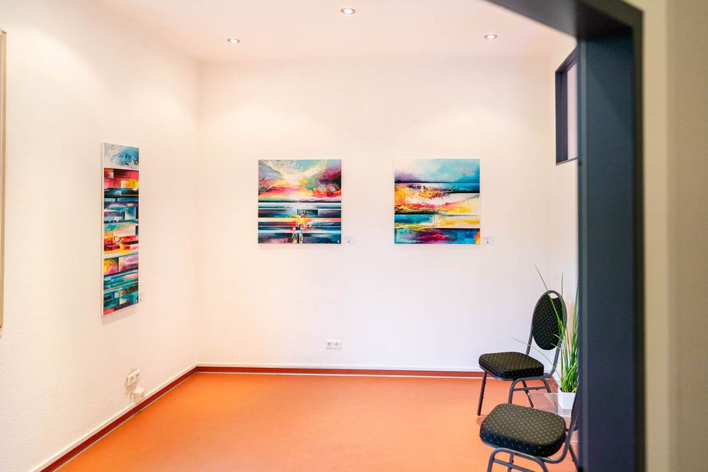 Art gallery interior with colorful landscape photographs displayed on white walls and modern office chairs.