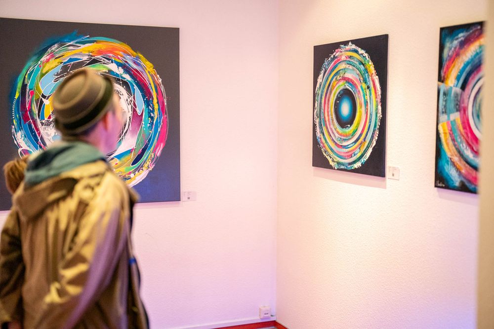 Colorful circular abstract art pieces displayed in a gallery with white walls and a viewer examining the artwork.