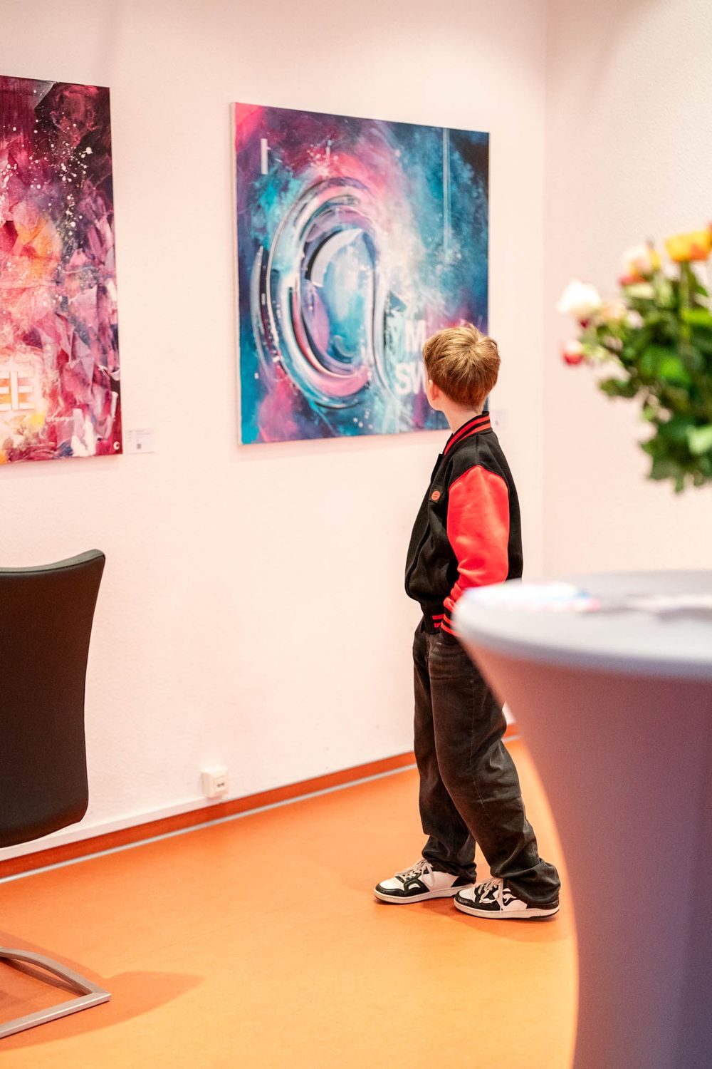 A person in black clothing views vibrant abstract art pieces displayed on a white gallery wall.