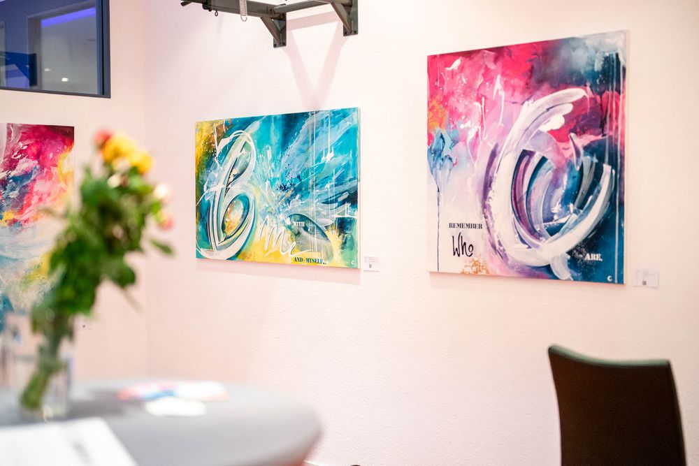 Colorful abstract artwork displayed on white walls in a modern gallery space with bright lighting.