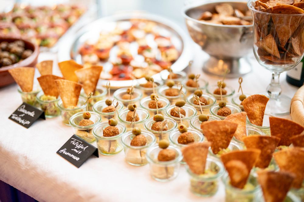 Elegant catering display featuring rows of appetizers, desserts and wine glasses on a white tablecloth at an upscale event.