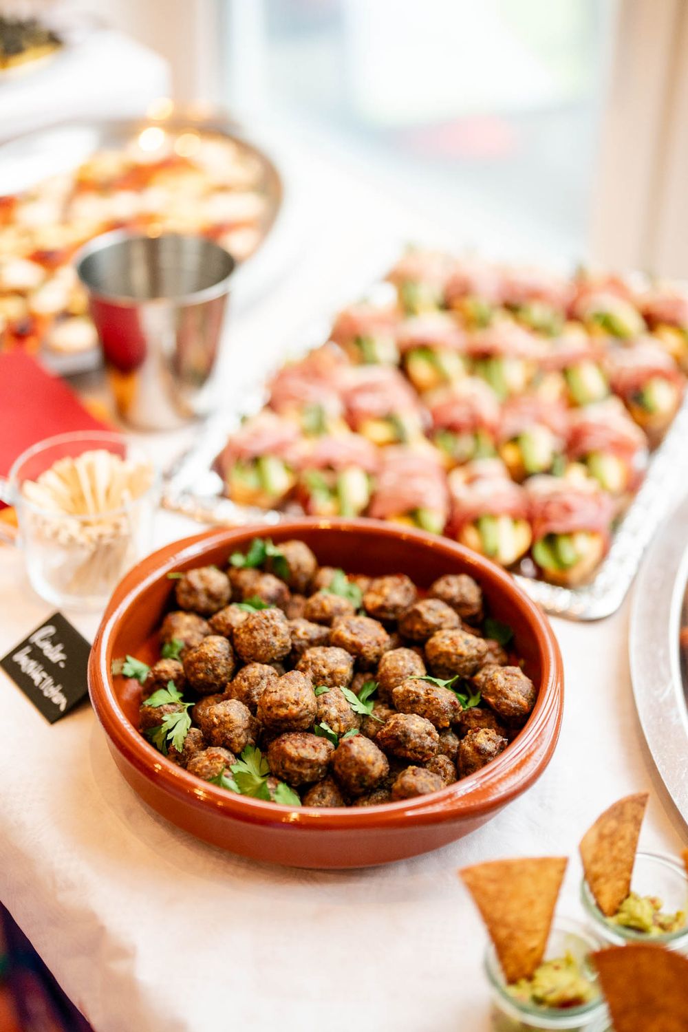 Terra cotta bowls filled with Spanish meatballs garnished with fresh herbs on a white buffet table.
