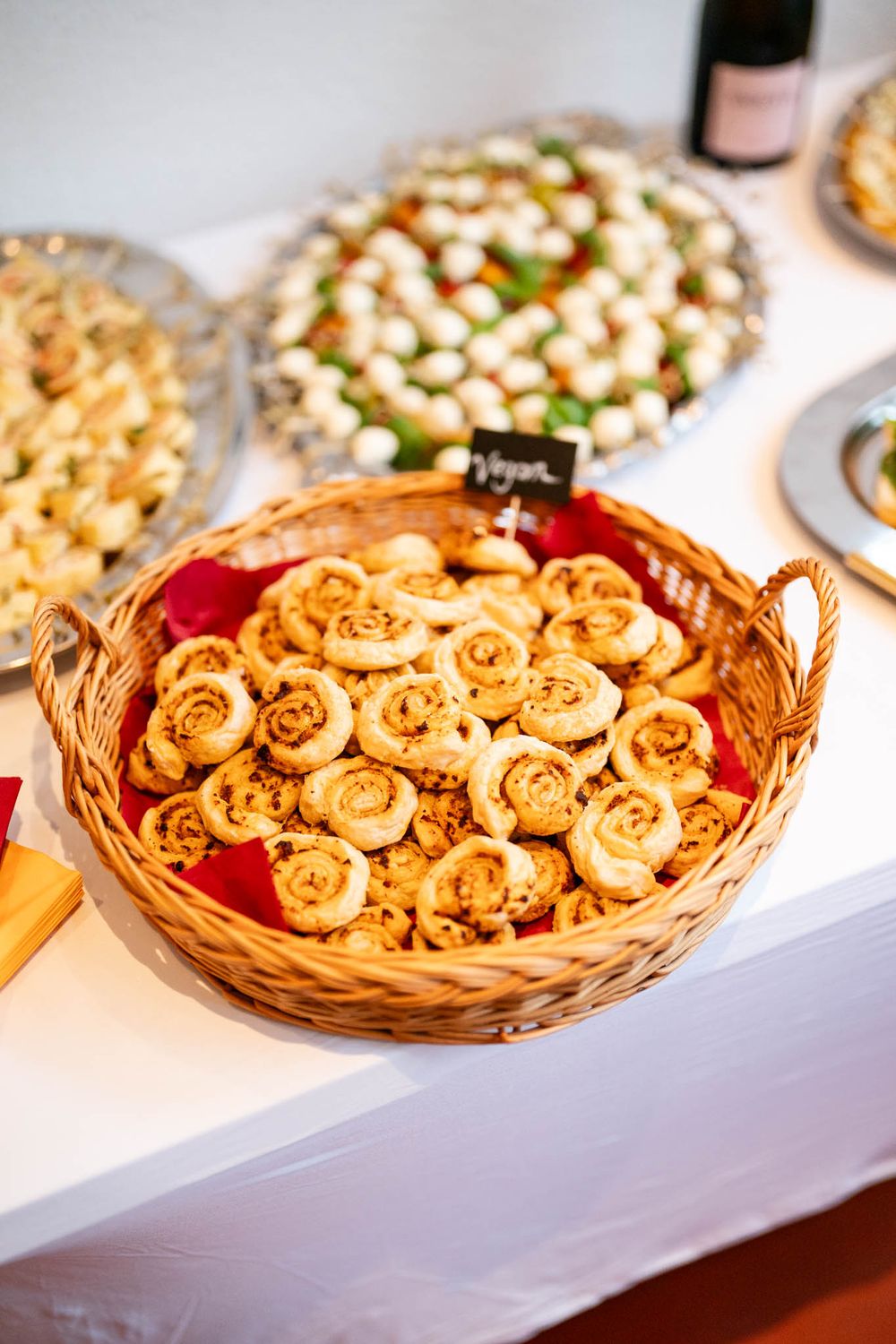 Golden brown pastry pinwheels arranged in a woven basket on a white tablecloth at a catering event.