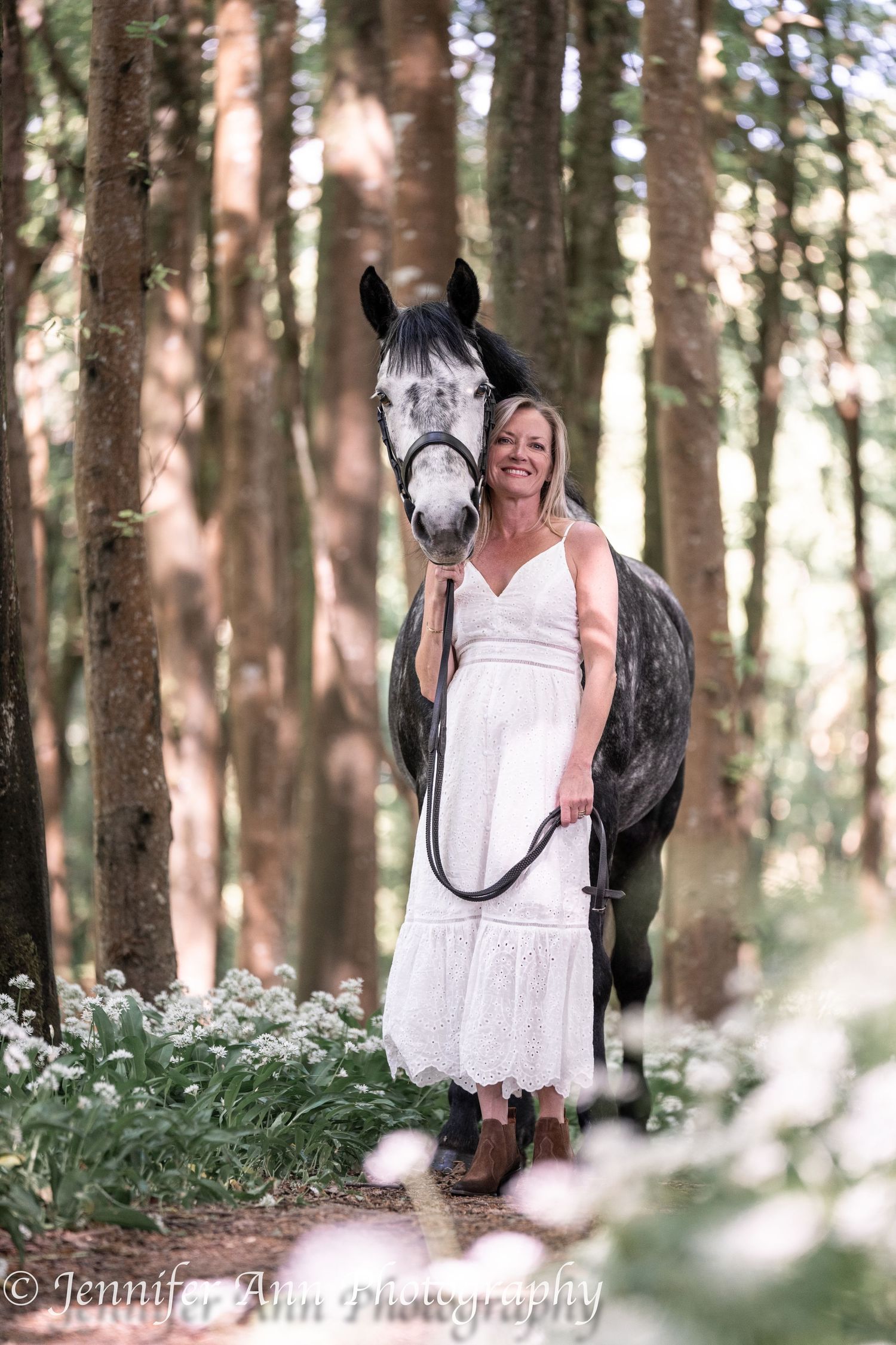 A series of dreamy forest photos showing a person in a white dress with a dark horse among blooming wildflowers.