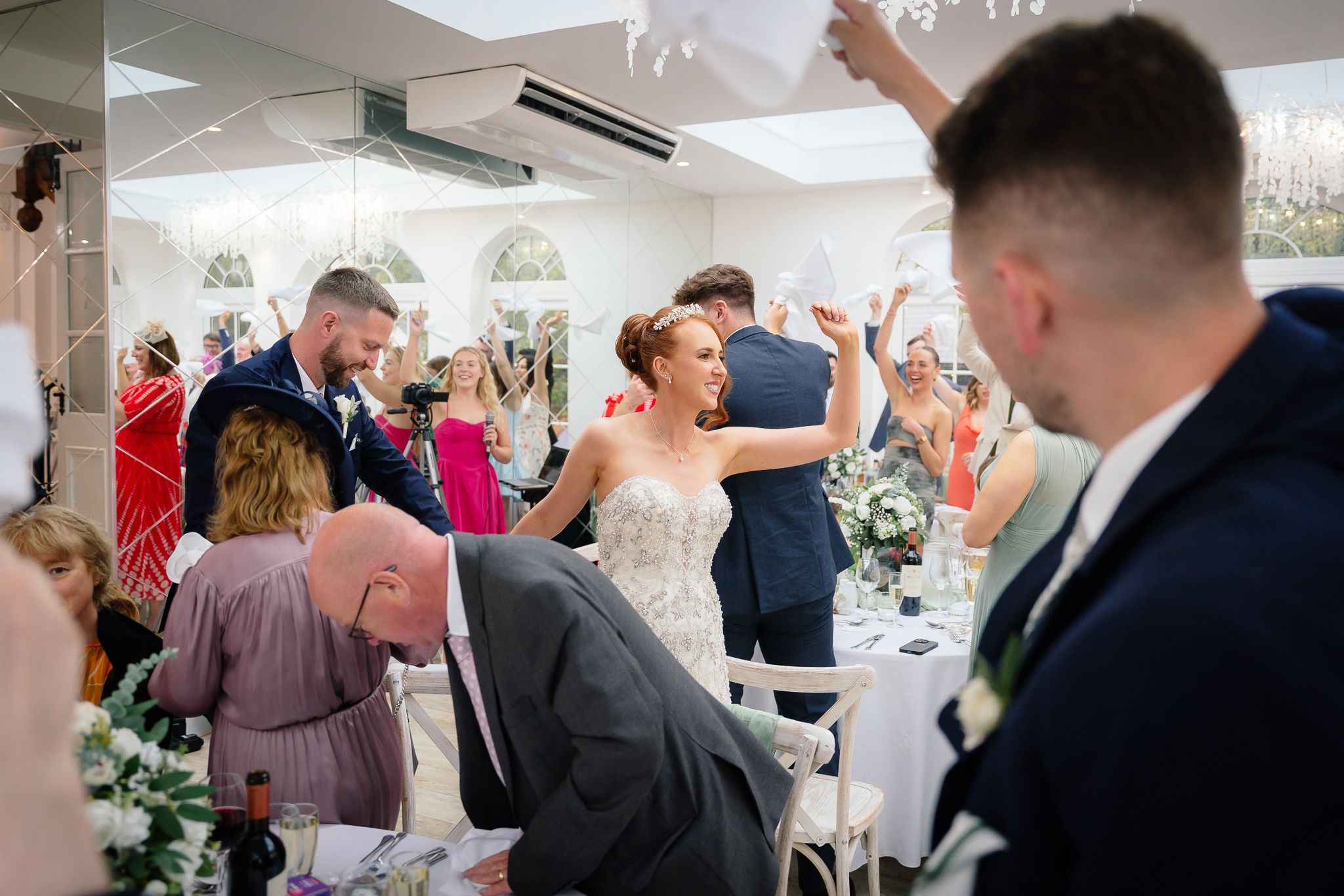 Wedding celebration inside bright reception venue with guests enjoying festivities. Woodhill Hall.