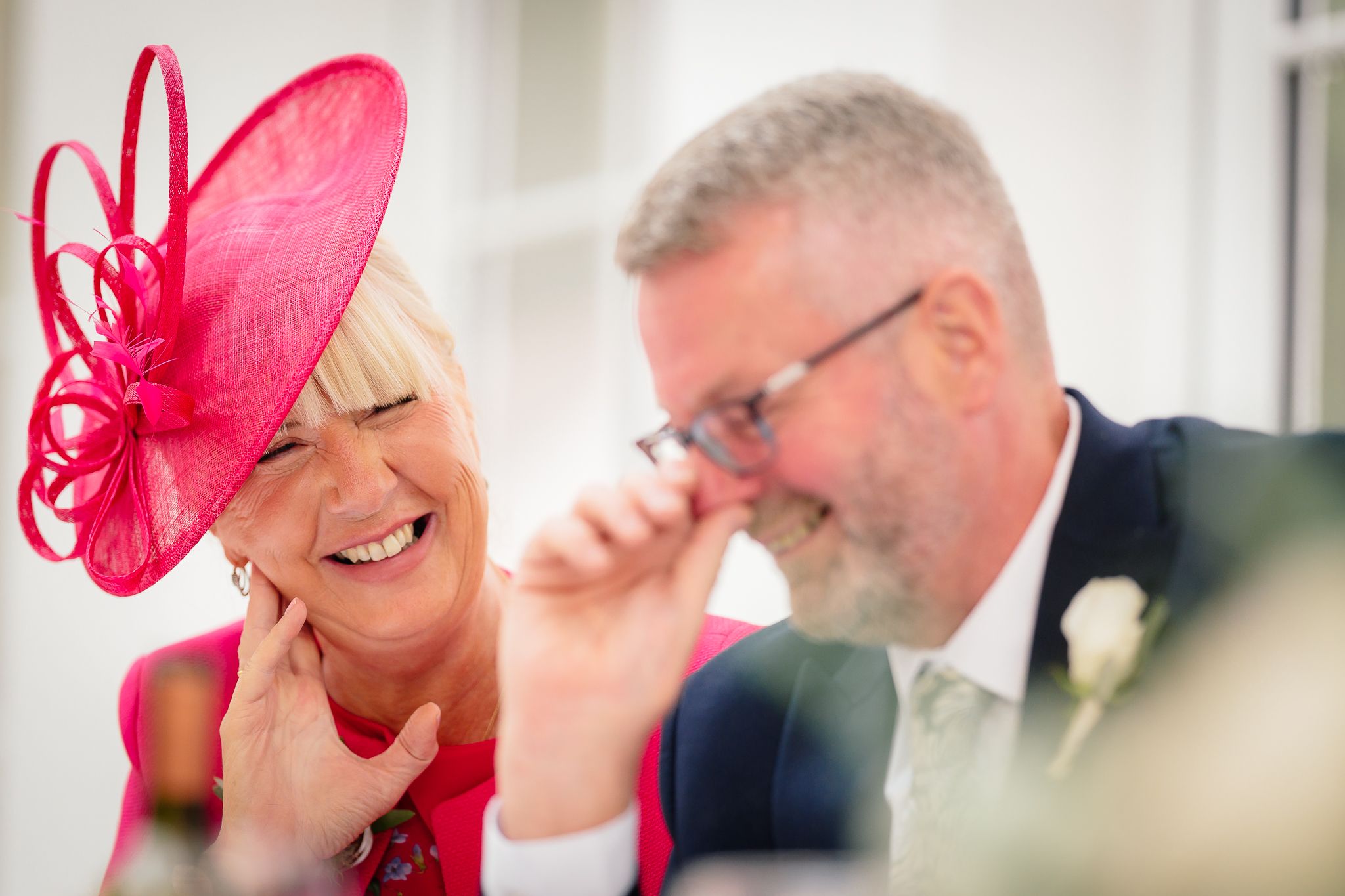 Wedding guests wearing bright pink fascinators during an indoor celebration. Woodhill Hall.