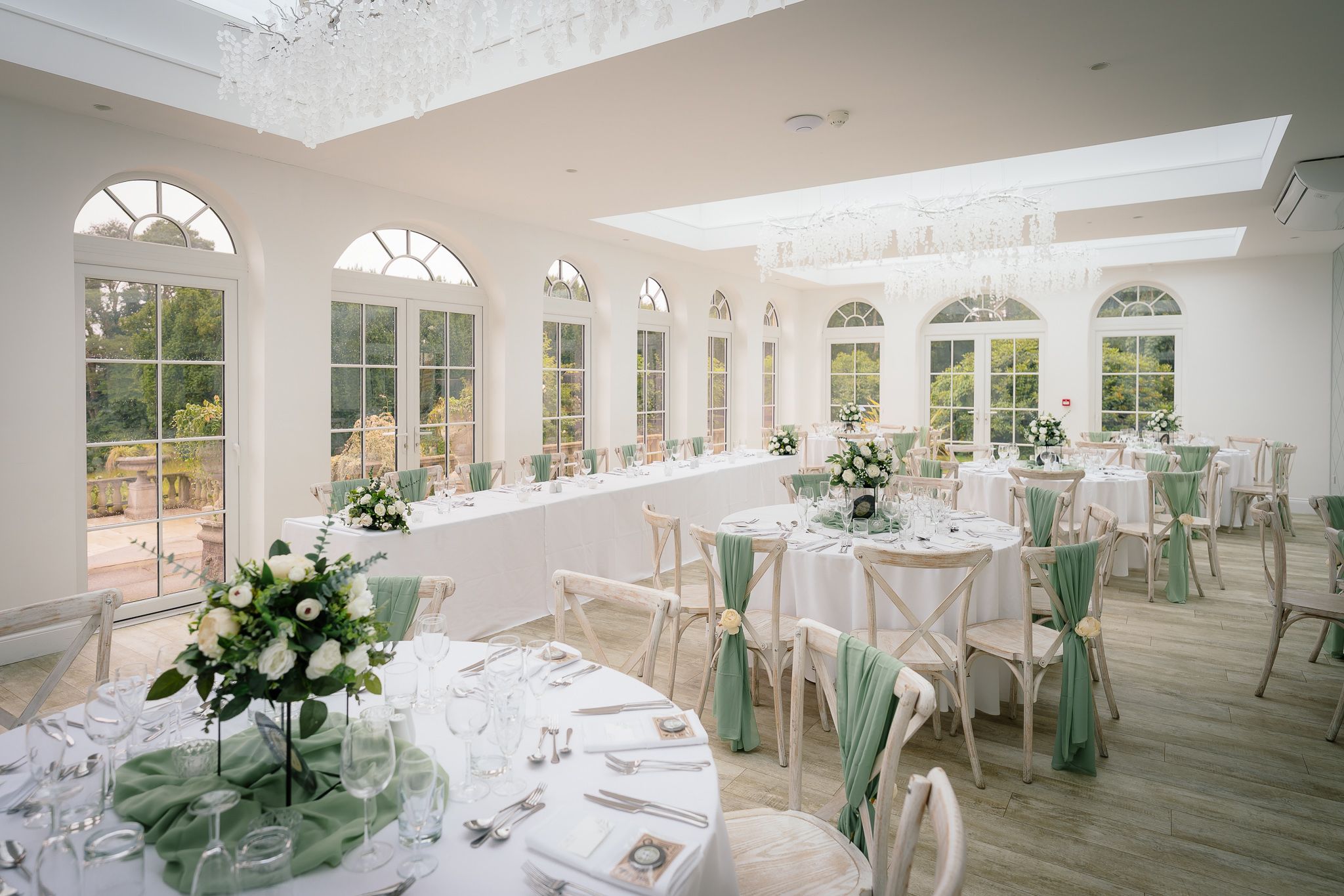 Elegant white wedding reception venue with arched windows, skylights and floral centerpieces on round tables. Woodhill Hall.