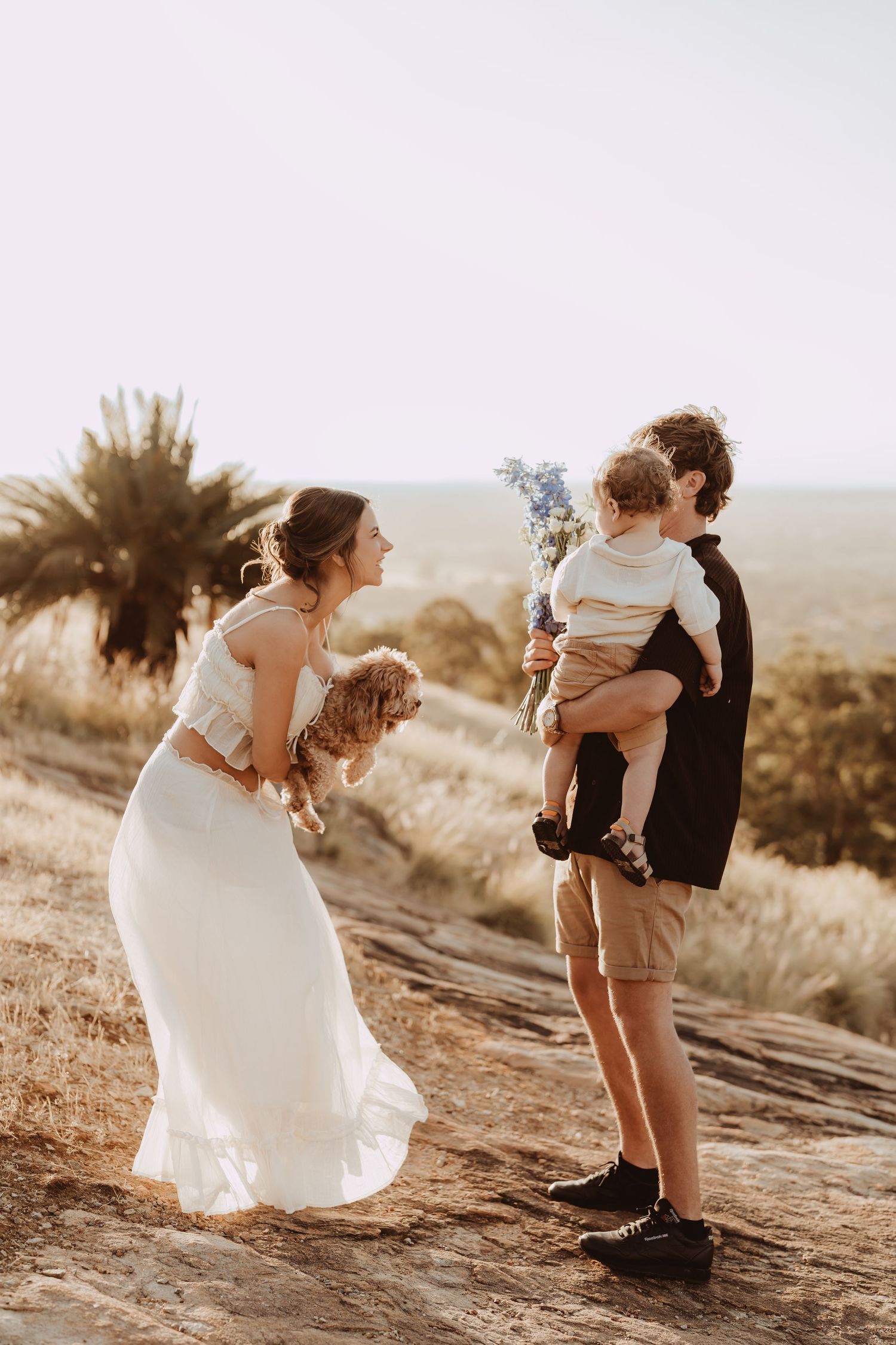 Couple in wedding attire shares intimate moments on a rocky hillside during golden hour sunset.