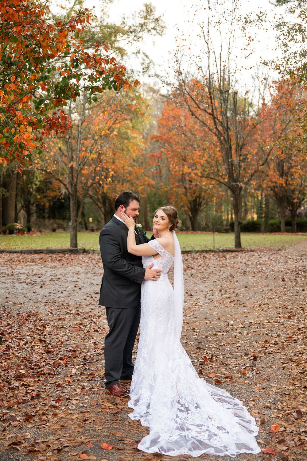Wedding portraits on carpet of autumn leaves with beautiful fall colors in background.