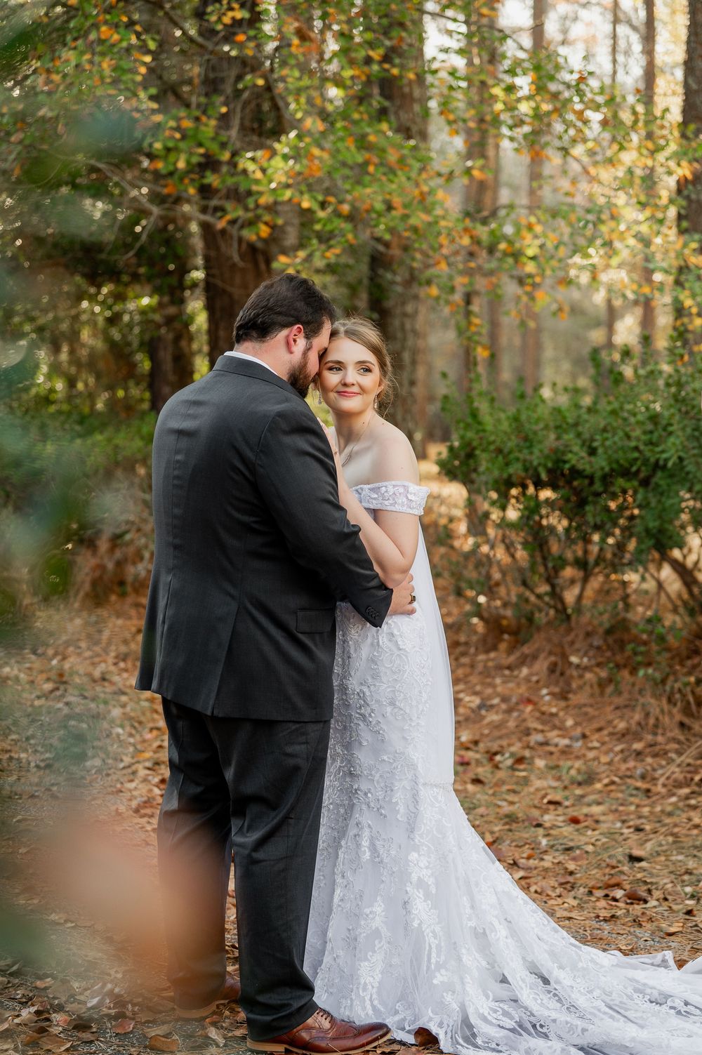 Elegant wedding photography featuring a lace dress with long train in a wooded autumn setting.
