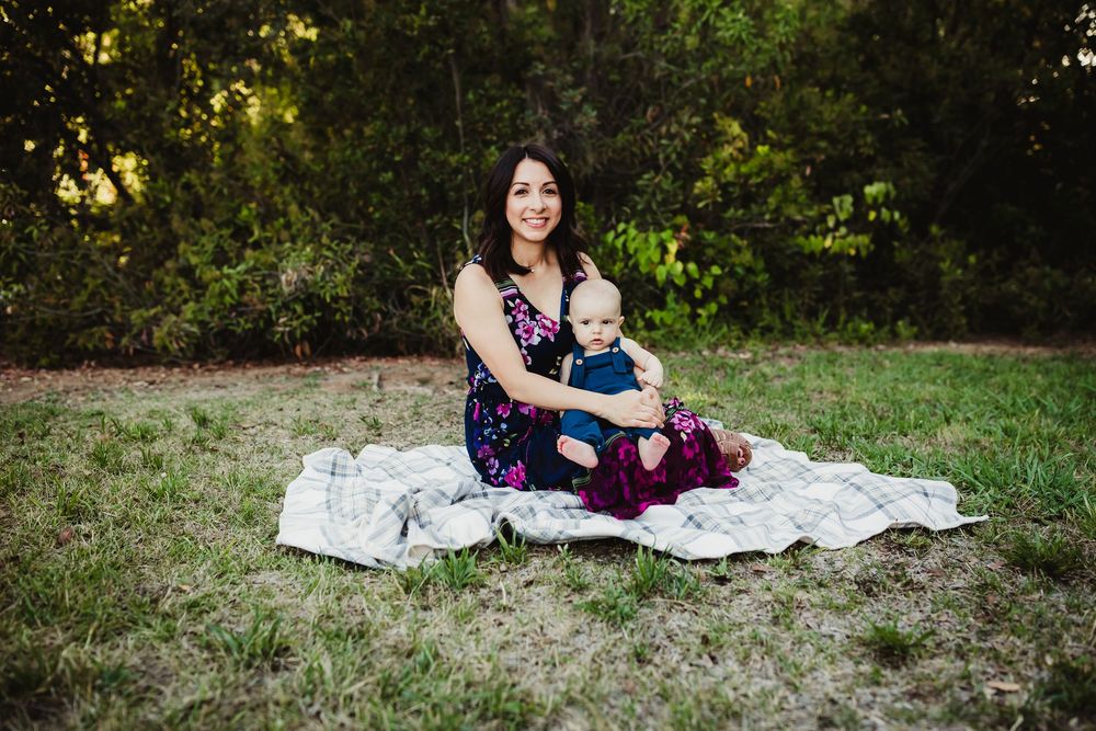 A family sits together on a white blanket in a sunlit outdoor setting during a photo session.