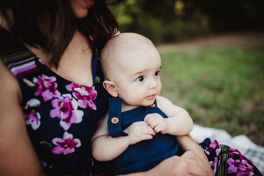 A tender parenting moment captured in natural outdoor lighting with greenery in the background.