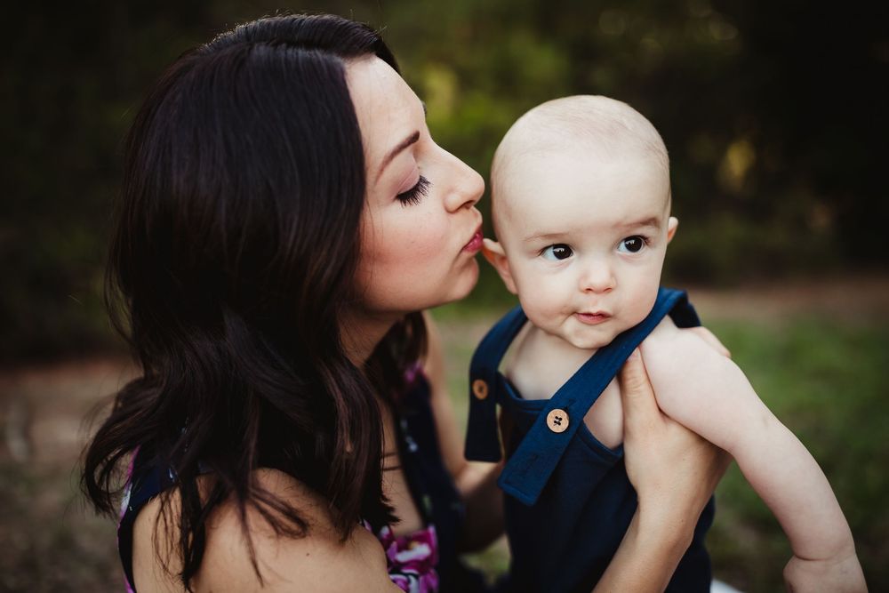 A tender outdoor family portrait session shows a mother and baby on a blanket in warm golden light.