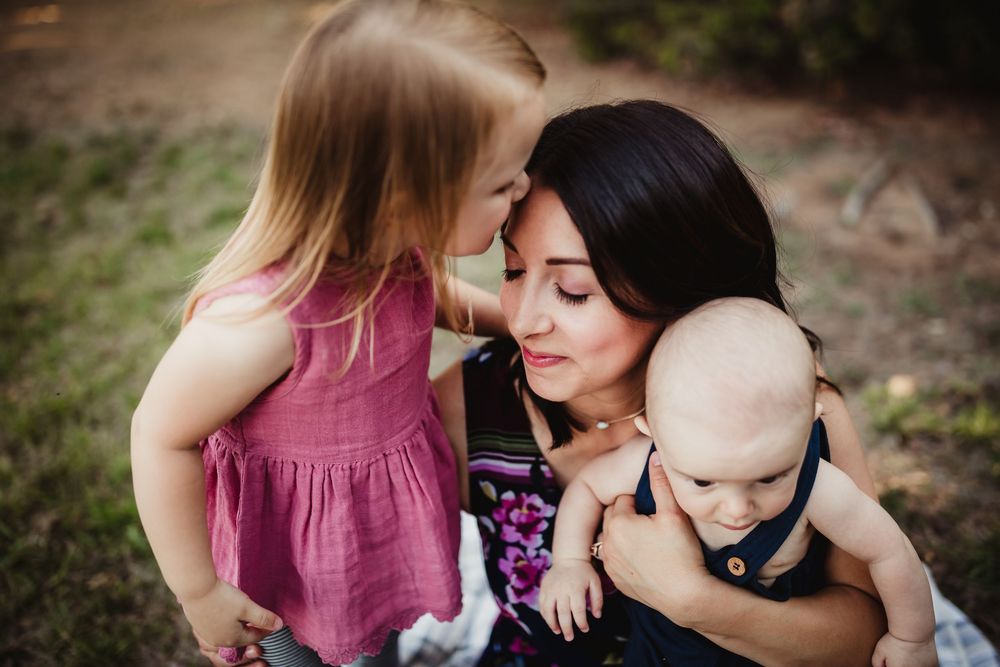 A tender moment captured outdoors with gentle embraces and pink clothing against a natural background.