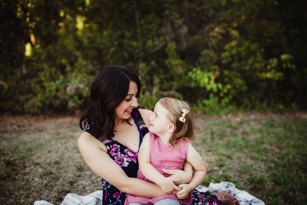 A tender moment captured between family members sitting on a blanket in a natural outdoor setting.