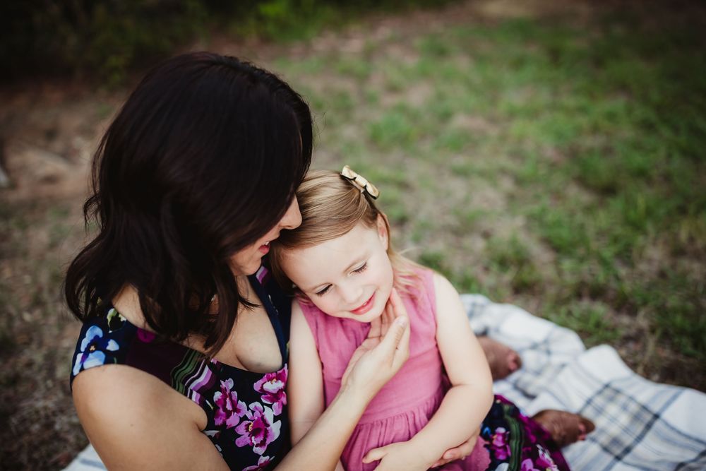 An intimate portrait of affection between family members sitting together on a blanket outdoors.