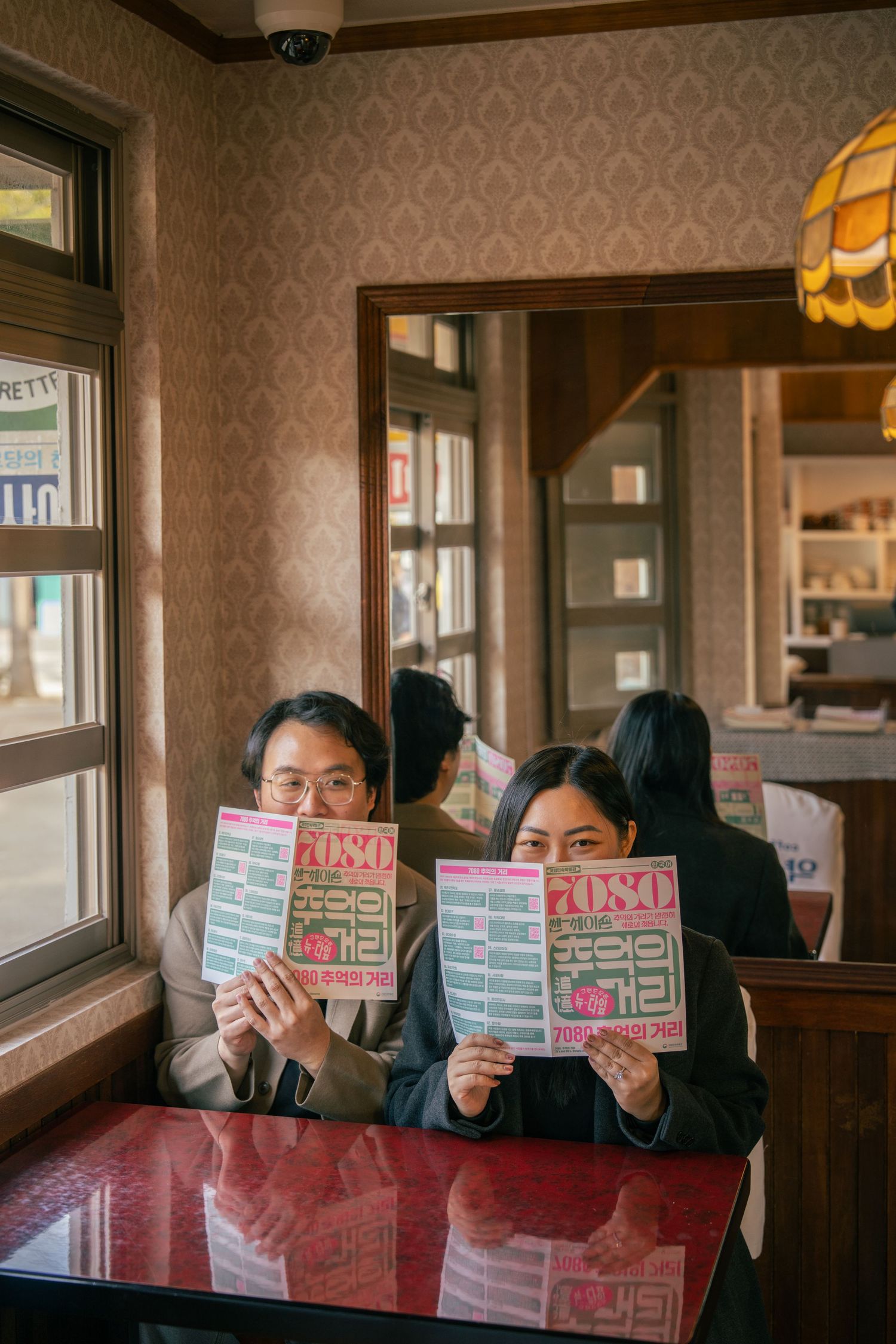 A sequence of four photos showing someone holding up colorful paper signs while sitting in a restaurant booth.
