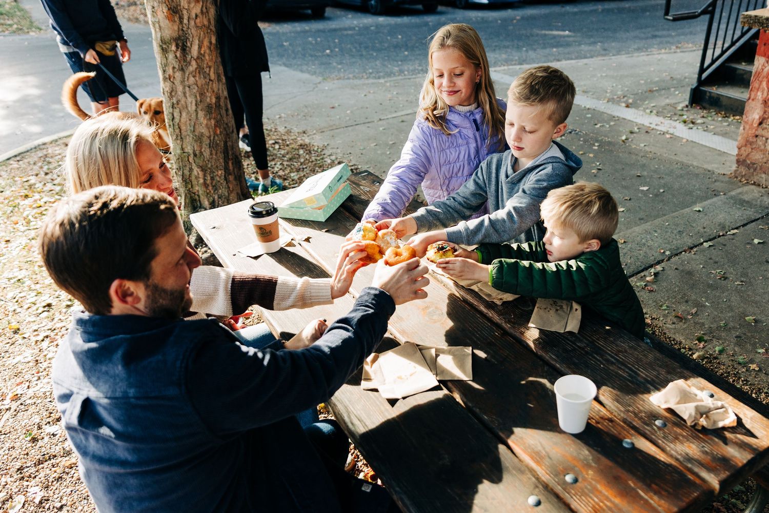 People enjoying doughnuts together at an outdoor restaurant table on a sunny day in Charlotte, NC.