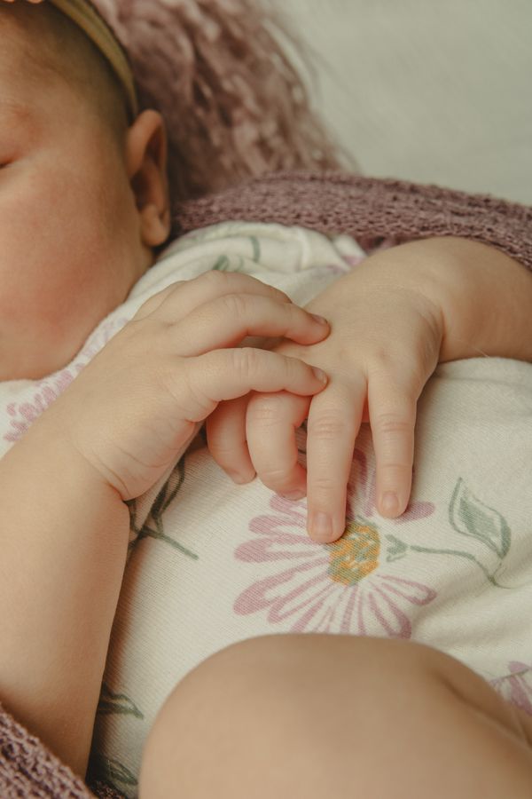 baby girl hands on her tummy wearing a white onsie with pink flowers