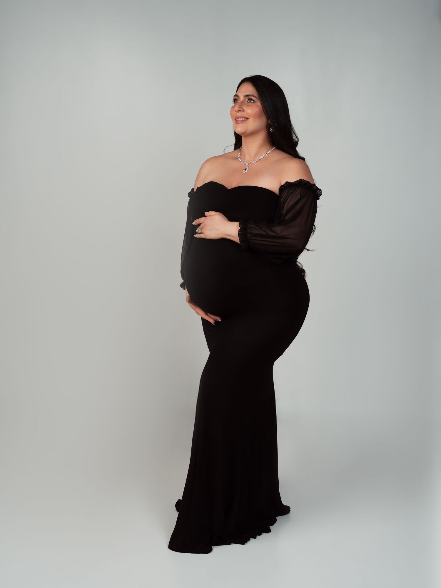 Model in white sweatshirt and black pleated skirt wearing long black gloves poses against light background.