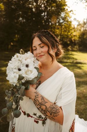 Person holding white floral bouquet with visible tattoo art in golden sunlight.