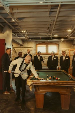 A group plays pool in formal attire at a reception venue with multiple billiards tables.