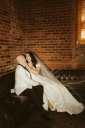 A flowing white wedding dress draped across a leather couch against exposed brick walls.