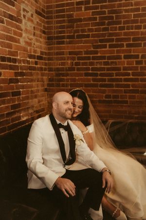 A romantic wedding couple shares an intimate moment against a rustic brick wall backdrop.