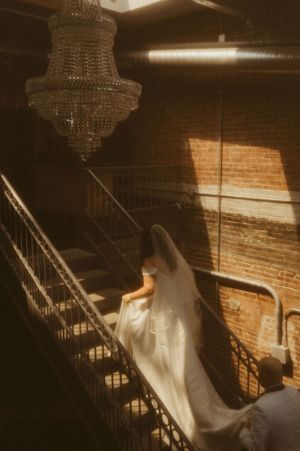 Ethereal scene of light streaming through a window onto a flowing white dress on a spiral staircase.