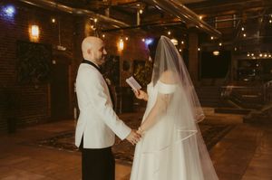 A couple exchanges vows during an intimate indoor wedding ceremony with warm lighting and exposed brick walls.