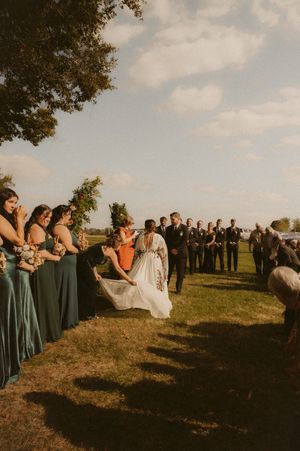 Wedding party in sage green dresses gathered outdoors during golden hour.