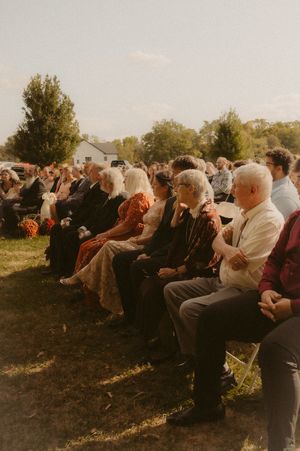 Guests seated in chairs outdoors at a sunset wedding ceremony with golden light filtering through trees.
