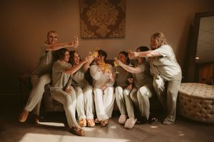 Group of people in white outfits sitting casually together against a wall in warm indoor lighting.
