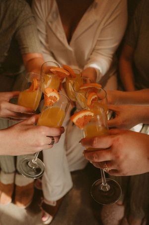 Hands toasting with orange cocktails in elegant glasses at a celebration.