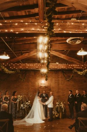 Wedding ceremony in a rustic brick venue with exposed beams and string lights creating warm ambiance.