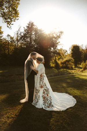 A romantic sunset wedding portrait shows a couple embracing in a golden field with flowing white lace dress and veil.