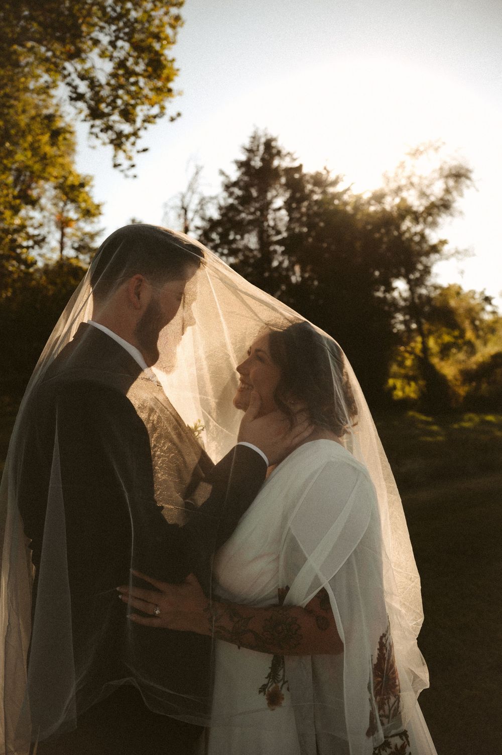 Silhouetted couple sharing an intimate moment at sunset with a flowing veil catching the golden light.