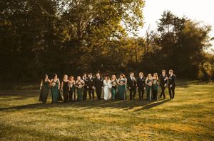 Wedding party poses in a line against golden sunset light in an outdoor field setting.