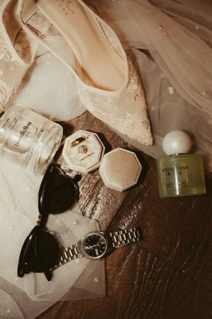 Wedding accessories including shoes and jewelry arranged on a dark wooden surface.