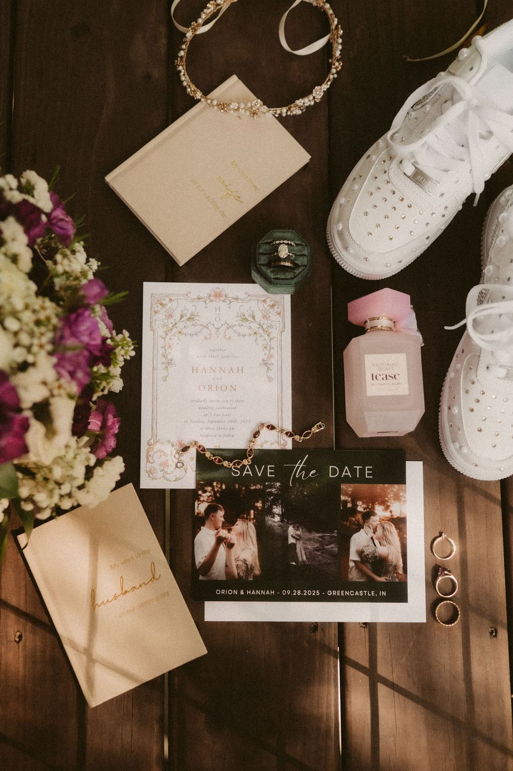 Wedding details flatlay with invitations, white sneakers, perfume, rings and flowers on wooden surface.