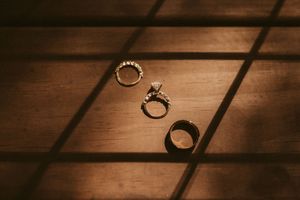 Wedding rings are photographed in a creative sequence against a dark wooden background in dramatic lighting.