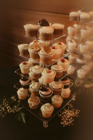 Elegant display of cupcakes arranged on tiered stands with floral decorations at a wedding reception.