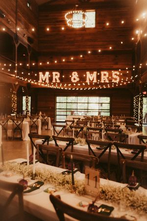 Rustic barn wedding reception venue with string lights and 'MR & MRS' sign on wooden walls.