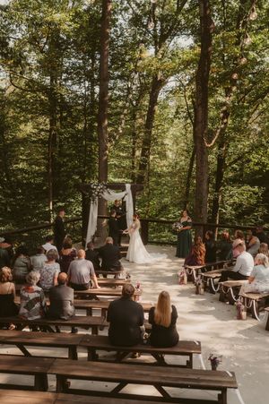 Wedding ceremony setup in a wooded area with wooden benches arranged for guests in natural outdoor setting.
