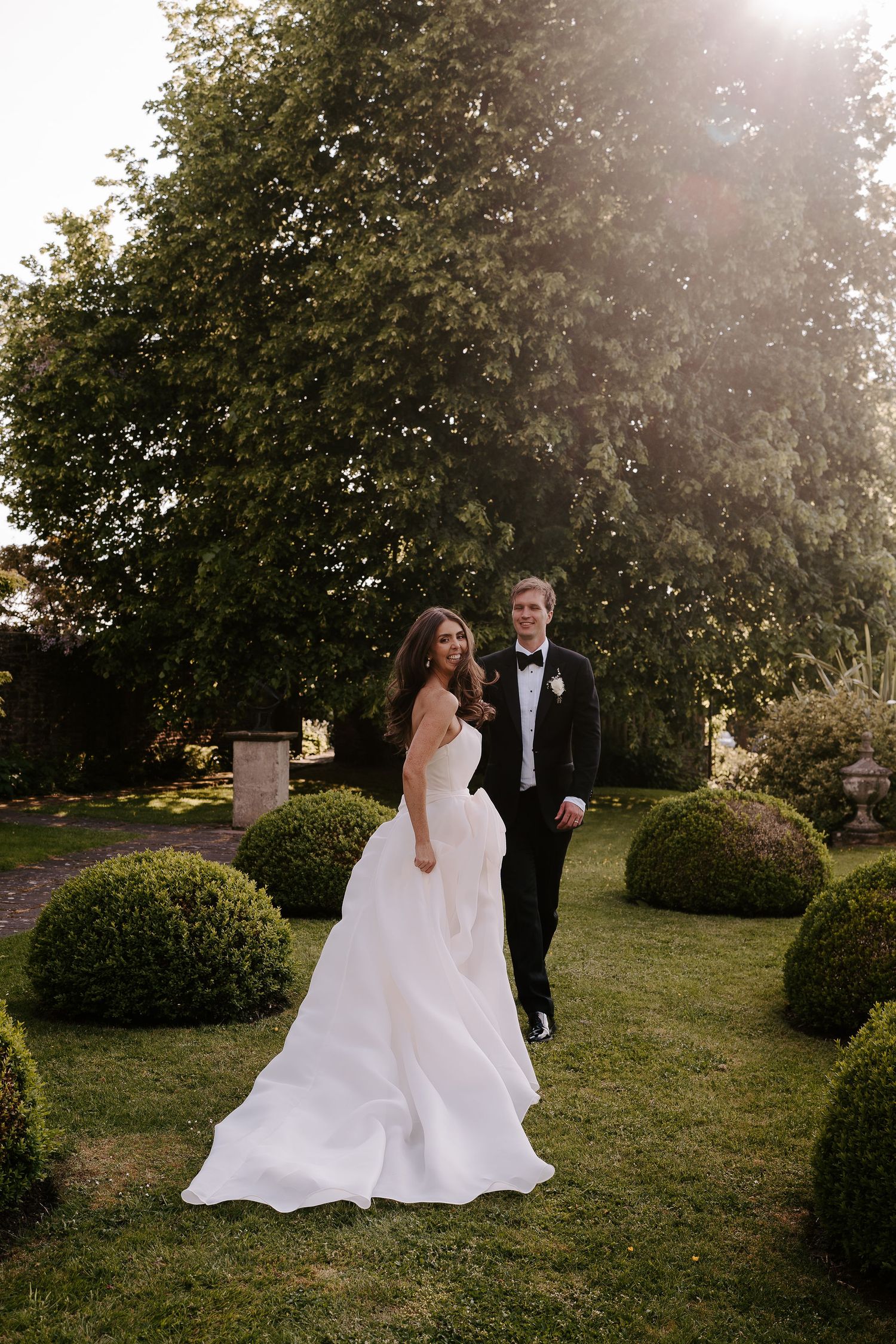 groom leading bride across lawn as bride laughs, looking over her shoulder at dewsall court in herefordshire