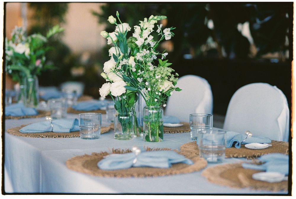 Elegant wedding reception table with white floral centerpieces, burlap chargers, and glassware on a light blue linen.