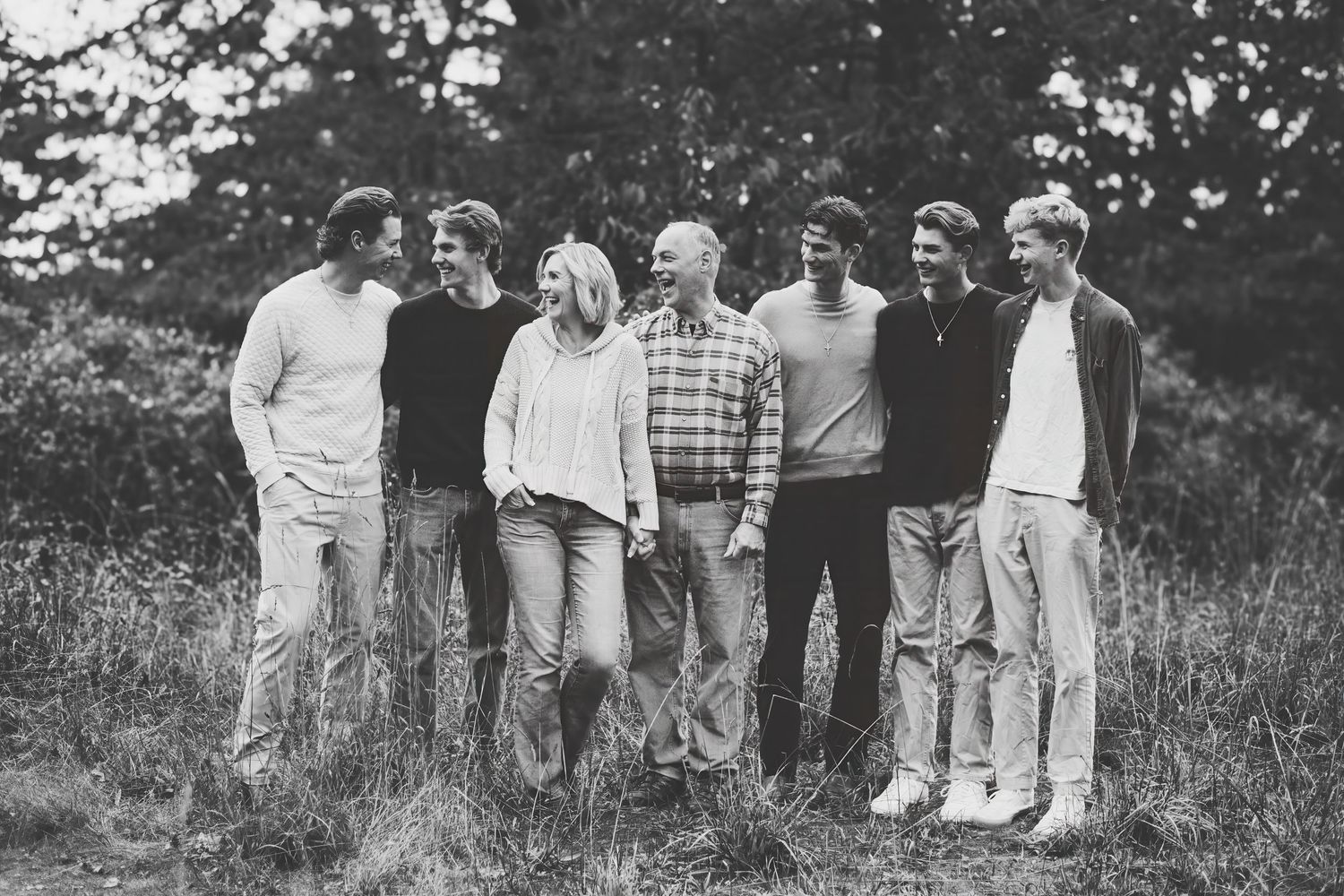A vintage black and white photograph shows a group of people standing in a grassy field on a sunny day.