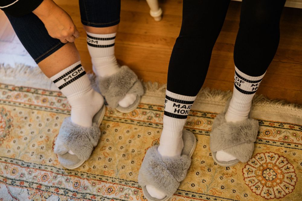 Several pairs of feet wearing cozy gray slippers and black socks lined up on a patterned carpet.