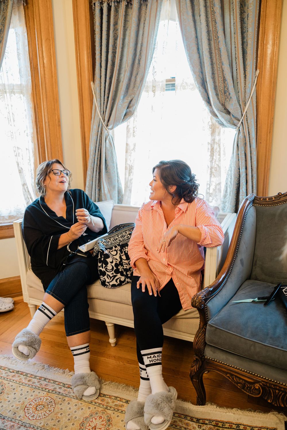 Two people sitting and chatting on an elegant couch in a room with ornate curtains.