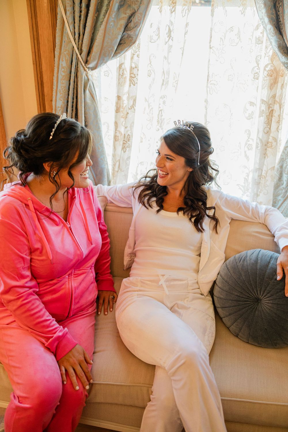 Two people in contrasting pink and white outfits sharing a joyful moment on a couch.